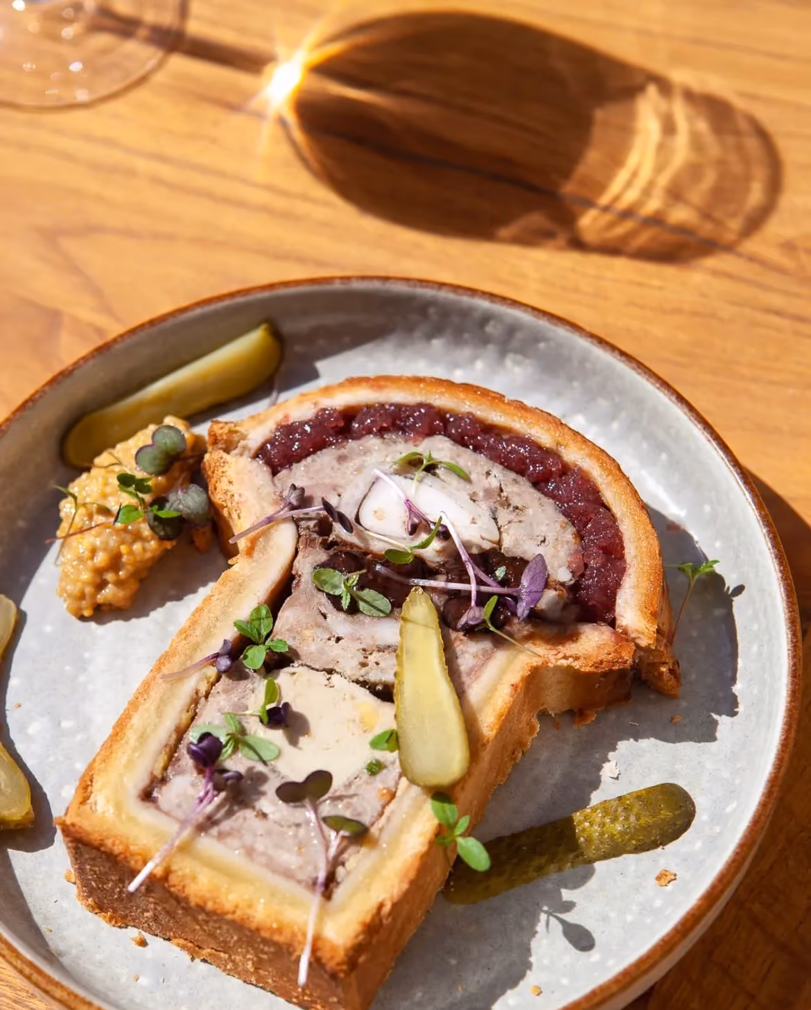 Pâté en croûte tranché sur une table en chêne au soleil, cornichons et moutarde